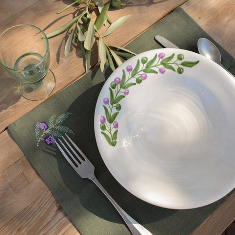 Table setting with a decorative plate, fork, spoon, and glass on a wooden table.