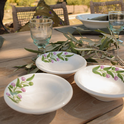 Outdoor setting with decorative bowls and glasses on a wooden table, surrounded by greenery.
