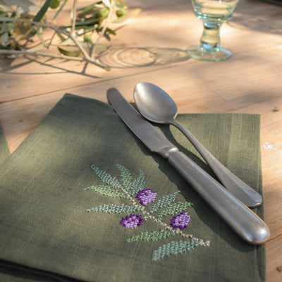 Green embroidered napkin with cutlery on a wooden table