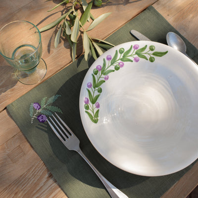 Table setting with a decorative plate, fork, spoon, and glass on a wooden table.
