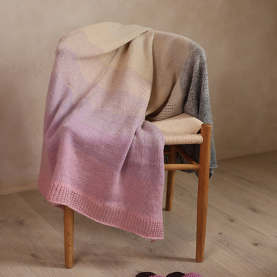 Pink and beige blanket draped over a wooden stool on a wooden floor.