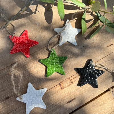Star-shaped ornaments in red, green, white, and black on a wooden surface with leaves in the background.